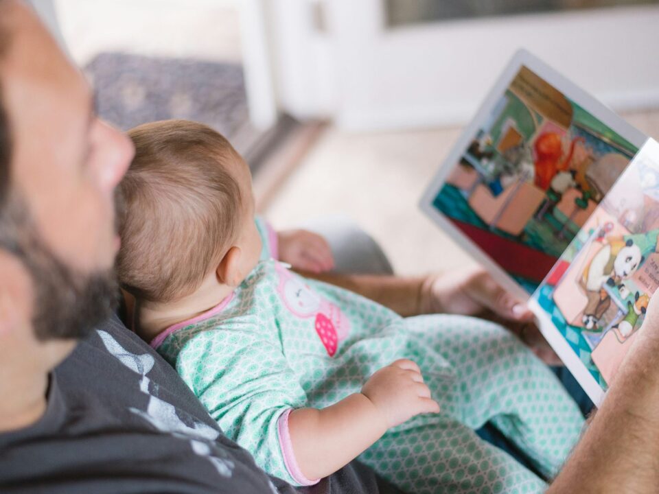 Padre leyendo un cuento ilustrado con su bebé en brazos