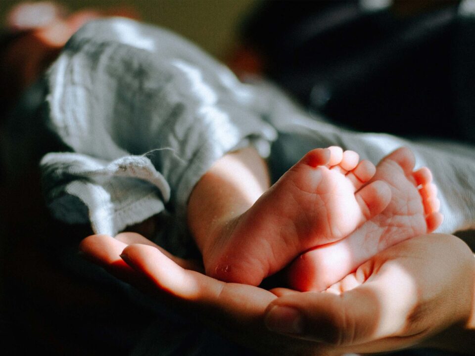 Manos de un adulto sosteniendo con cuidado los pies de un bebé